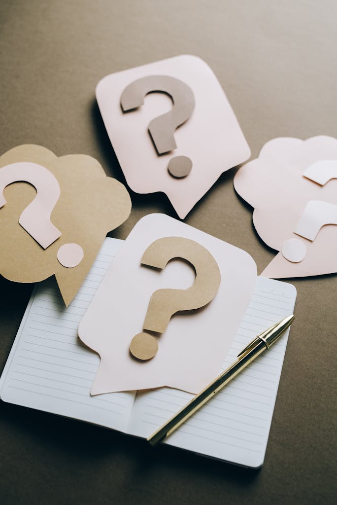 Artistic paper question marks on an open notebook with a pen, symbolizing curiosity and creativity.
