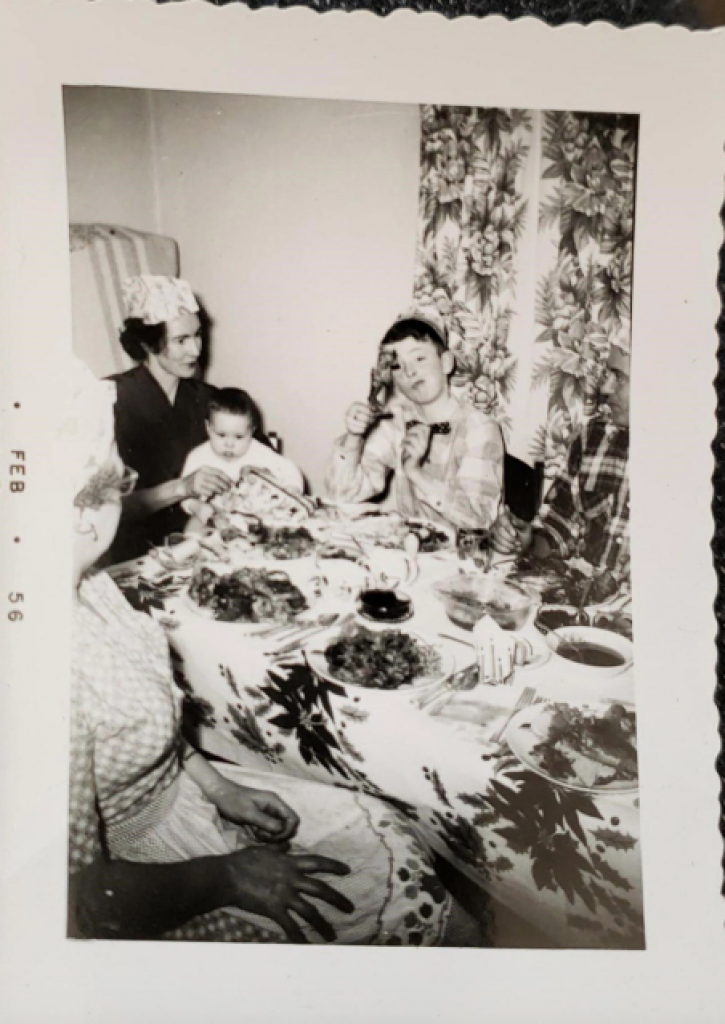A Christmas scene from 1956 that features my grandma with a baby on her lap, and my dad wearing a Christmas hat.