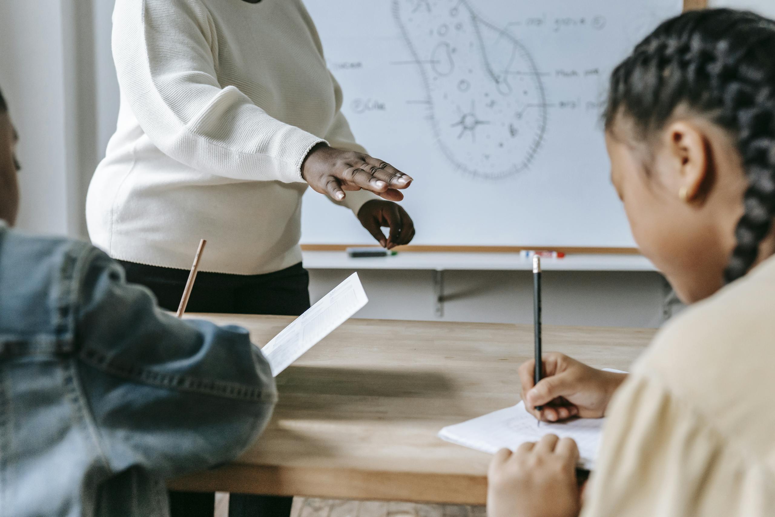 Teacher guides students through a lesson in a classroom. Focus on writing and learning.